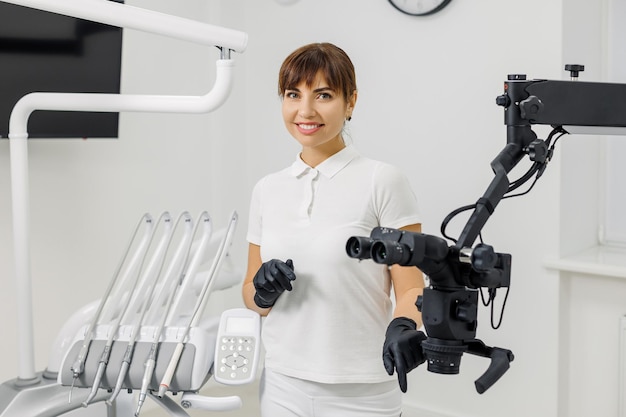 사진 혁신적인 현미경 근처 구강 클리닉에 서 있는 웃는 여자 치과의사