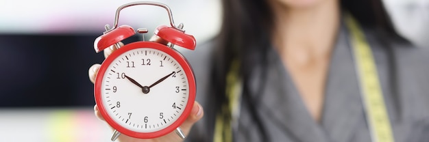 時間の概念の注文の赤い目覚まし時計の実行を保持している笑顔の女性デザイナースタイリスト