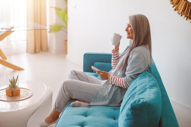 コーヒーを飲み、自宅で携帯電話を使用して笑顔の女性