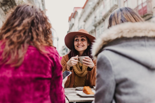 smiling woman drinking coffee while talking with friends in city