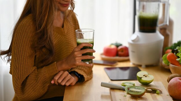 Smiling woman drinking green detox vegetable smoothie at home Healthy lifestyle concept