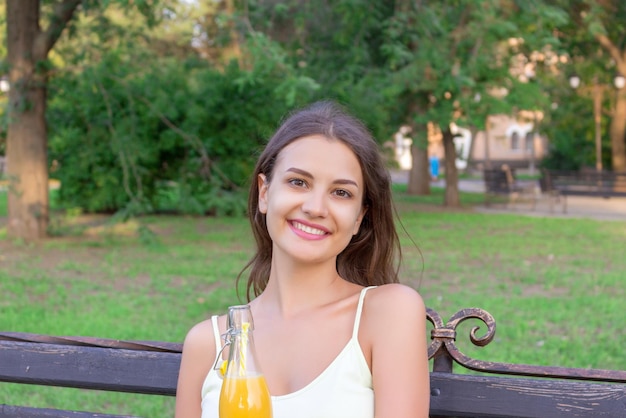 Smiling woman drinking juice while sitting in public park