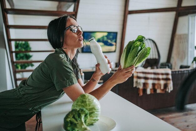 写真 家のキッチンで牛乳を飲み野菜を食べている笑顔の女性