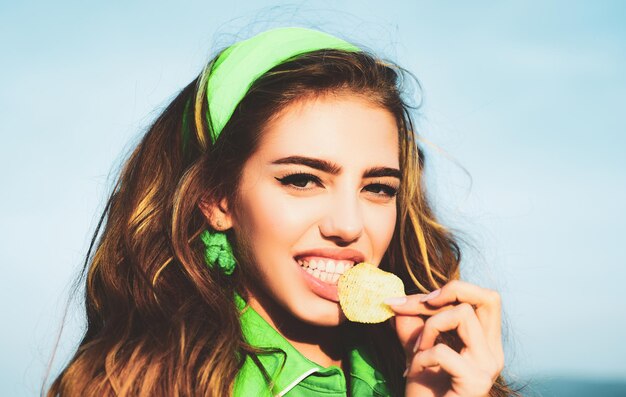 Smiling woman eat potato chips young woman biting piece of potato chips with teeth tasty delicious f