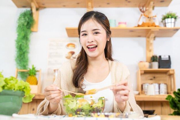 Smiling woman eating fresh healthy salad vegetables woman sitting at pantry in a beautiful interior kitchen the clean diet food from local products and ingredients market fresh