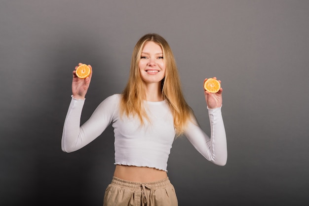 Smiling woman eating orange, half fruit, long hair. Studio shot