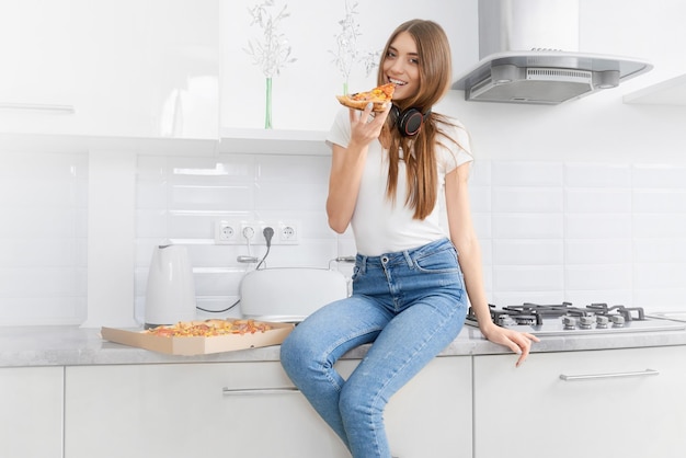 Smiling woman eating tasty pizza in kitchen