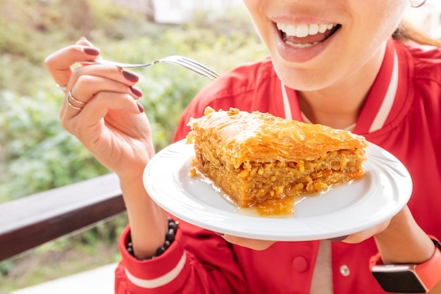 Foto la donna sorridente mangia il dessert dolce della pasta sfoglia con il baklava delle noci e del miele