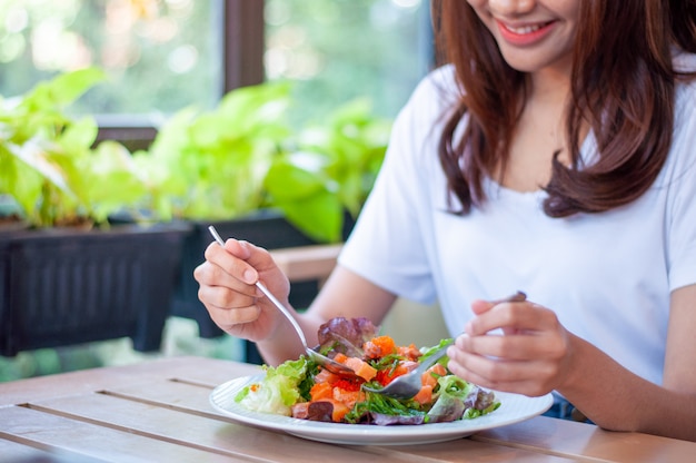 笑顔の女性は、サーモンサラダを食べることを楽しんでいます。体重とダイエットを減らすには、体に有益な食品を食べます。減量のコンセプトです。