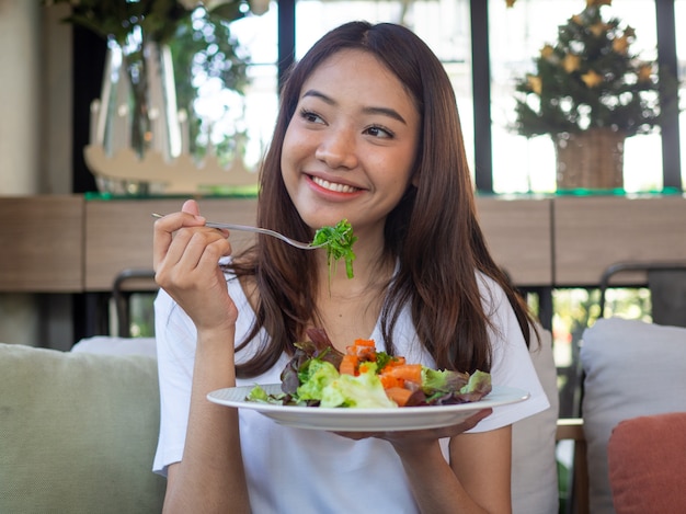 The smiling woman enjoys eating a salmon salad.