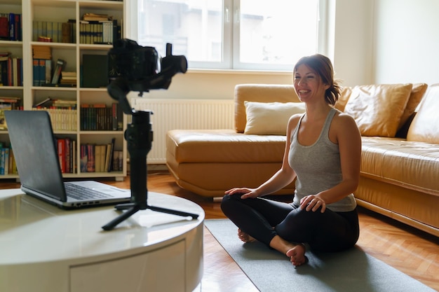 smiling woman filming while sitting on mat at home