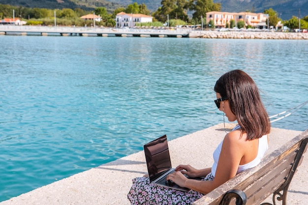 Smiling woman freelancer working on laptop outdoors at city harbor copy space