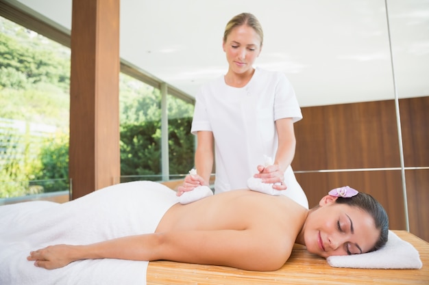 Smiling woman getting a back massage with herbal compresses