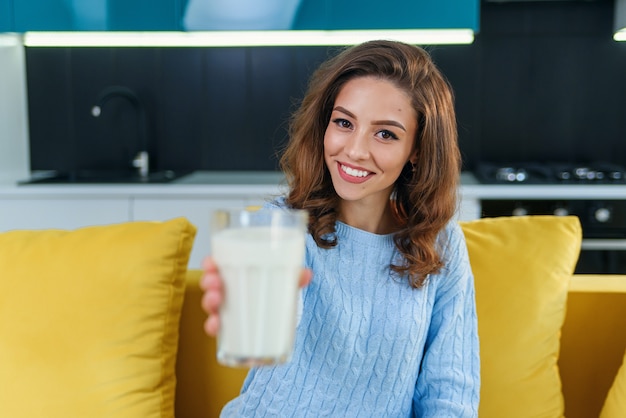 Smiling woman gives a glass of fresh milk in the stylish cozy kitchen at the morning. Pretty healthy girl holds a glass of fresh milk on foreground.