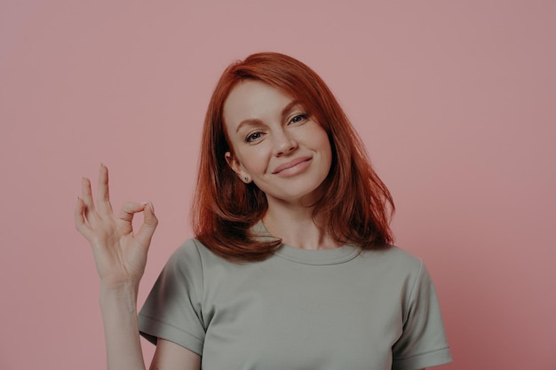 Smiling woman giving her approvalwhile posing isolated over pink studio background