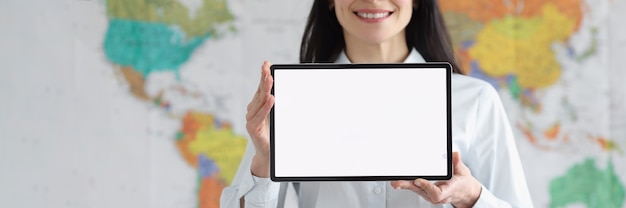 Smiling woman in glasses holds tablet with white blank screen on background of global map of world