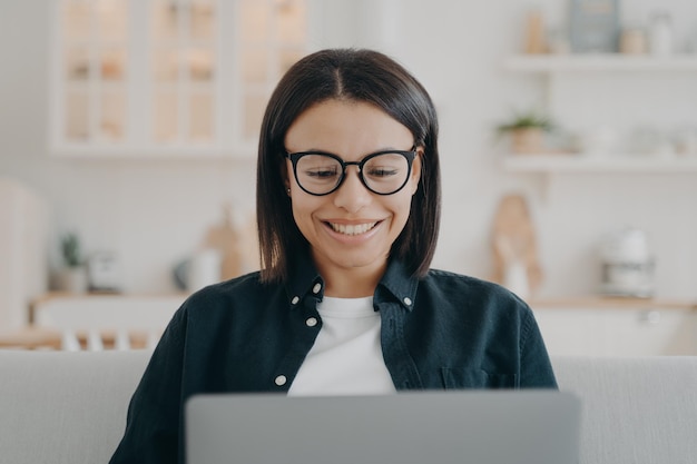 Smiling woman in glasses working at laptop learning online at home Distance work elearning