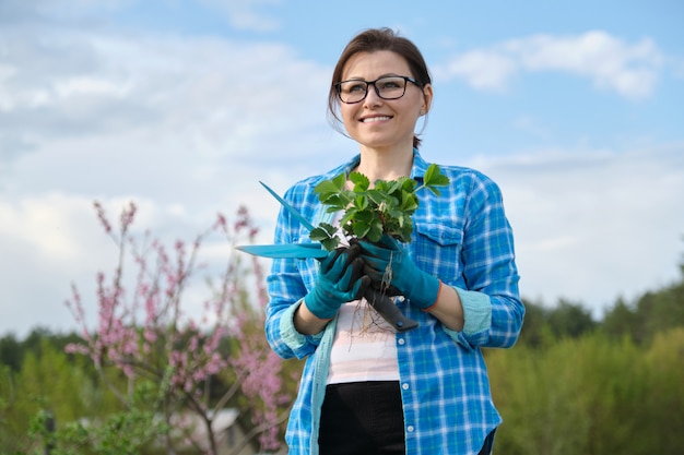 Smiling woman in gloves holding plant