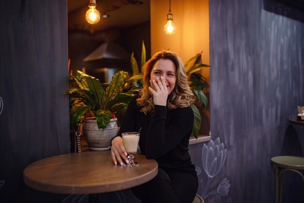 Smiling woman in a good mood with cup of coffee sitting in cafe\
dark interior evening gatherings in a cafe