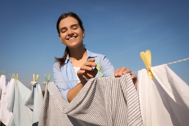 青い空を背景に乾燥するためのラインを洗濯に洗濯はさみで服をぶら下げ笑顔の女性