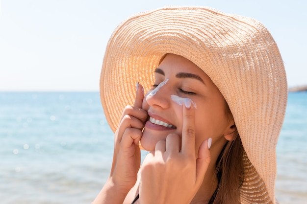 Smiling woman in hat is applying sunscreen on her face. Indian style.