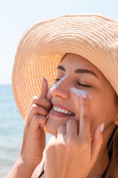 Photo smiling woman in hat is applying sunscreen on her face indian style