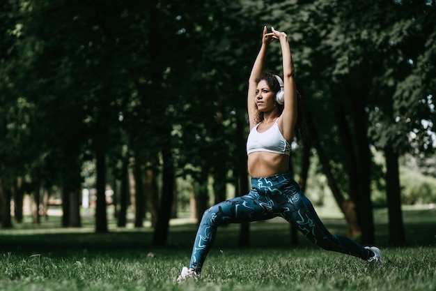 Smiling woman in headphones doing stretching before jogging outd