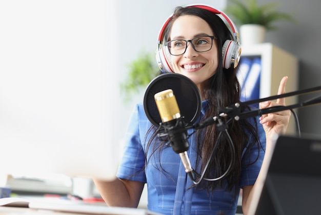 Smiling woman in headphones in front of microphone radio presenter and recording studio concept