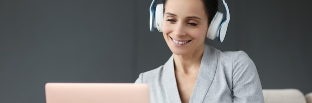 Photo smiling woman in headphones works behind laptop remote work concept