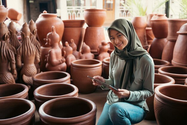 Smiling woman in hijab holding a pad between the earthenware