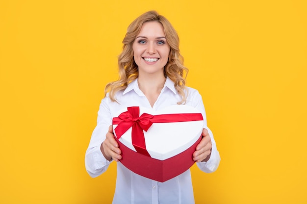 Smiling woman hold present heart box on yellow background