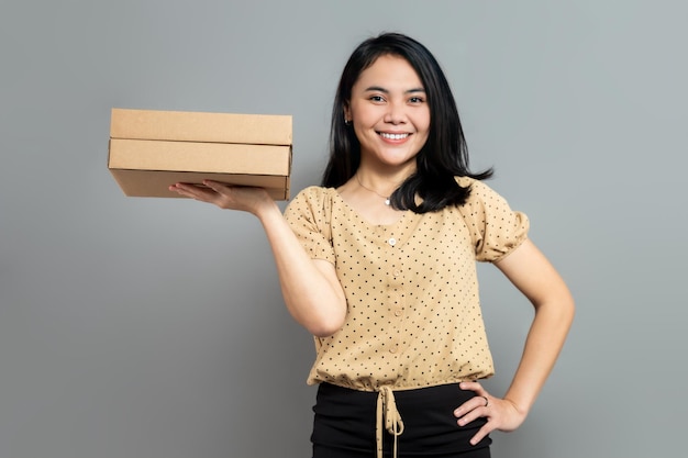 Smiling woman holding cardboard box with hands on waist