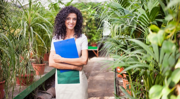 Smiling woman holding a clipboard in a greenhouse