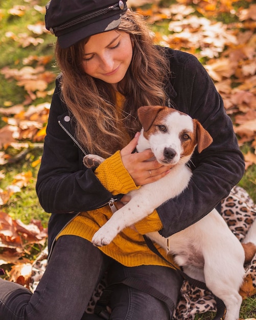 smiling woman holding dog sitting at park during autumn