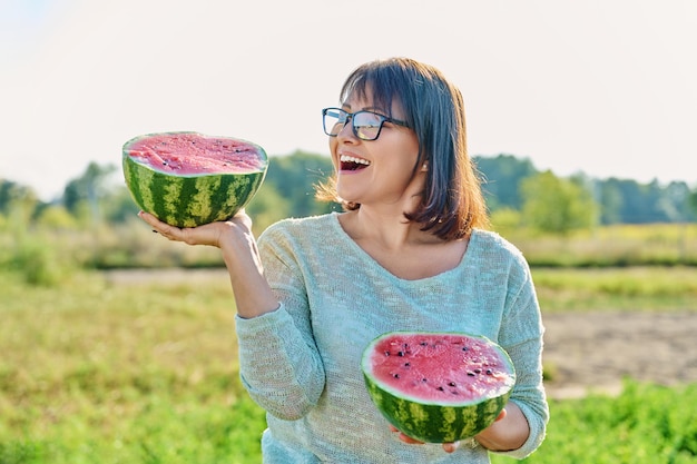 Photo smiling woman holding halves of ripe watermelon in hands outdoor