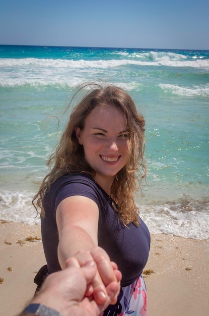 Foto donna sorridente che tiene la mano del fidanzato mentre è in piedi sulla spiaggia contro il cielo