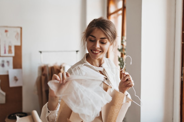 Smiling woman holding hanger with clothing pattern