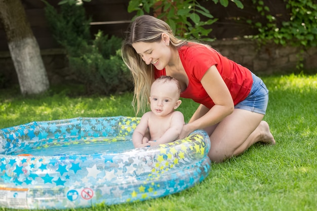 Donna sorridente che tiene il suo bambino in piscina gonfiabile in giardino