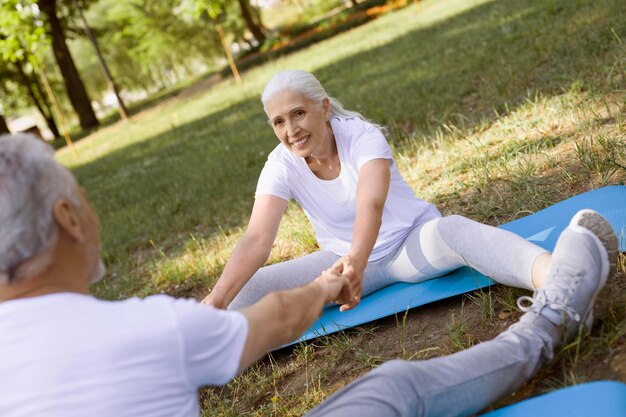 Smiling woman holding her husbands hands while doing stretching outdoors