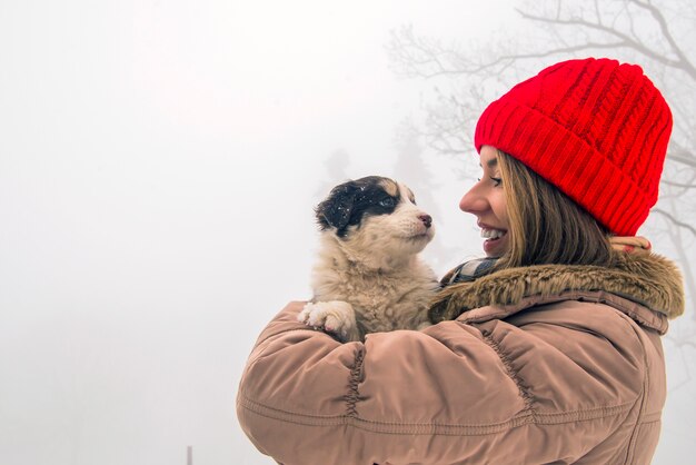 smiling woman holding her pet dog in his hands near face, hugging. Spitz breed dog playing with a woman walking outdoors winter day, warm clothing. love and care for the pet, dog walking