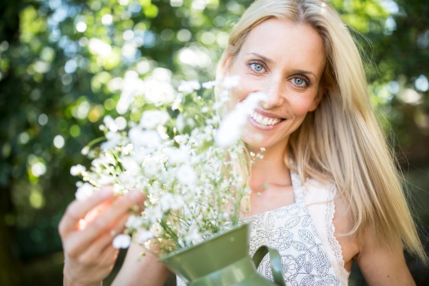 Photo smiling woman holding jug with flowers outdoors