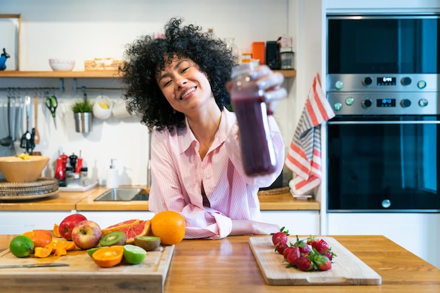 Smiling woman holding juice bottle at home