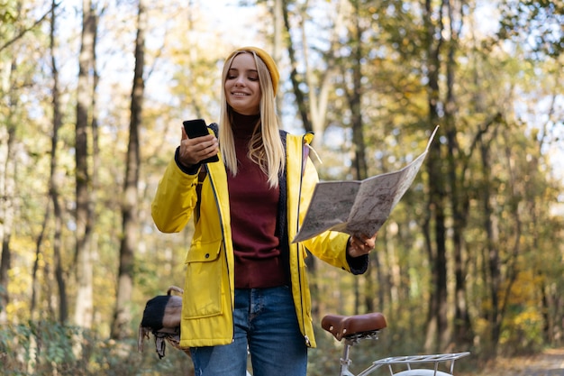 Donna sorridente che tiene il telefono cellulare utilizzando la mappa per navigare nella foresta autunnale viaggi in stile di vita attivo