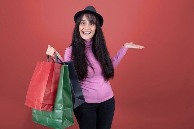 Smiling woman holding paper shopping bags wearing pink sweater and black hat isolated