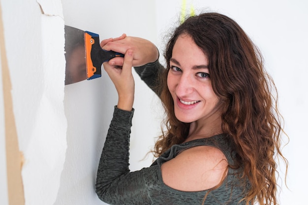 Smiling woman holding a scraper while removing wallpaper from a wall Home renovations