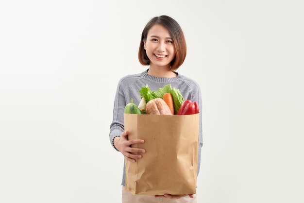 Smiling woman holding a shopping bag full of groceries posing on a studio white background