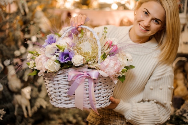 柔らかい白、ピンク、紫の花の籐のバスケットを保持している笑顔の女性