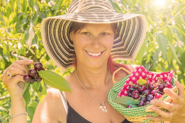 smiling woman holding wooden box with fresh ripe cherries