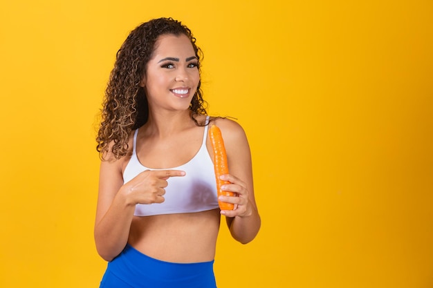 Smiling woman holds a carrot on yellow background.