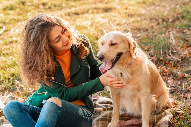 顔の近くで彼女のペットのゴールデンレトリバー犬を抱き締める笑顔の女性。晴れた日に屋外を歩く巻き毛の女性と遊ぶゴールデンレトリバー犬。ペットの愛と世話。